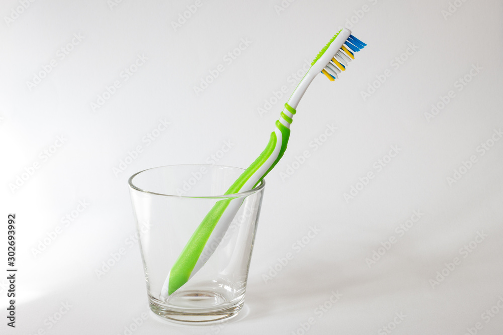 Close-up of a new and clean toothbrush in a transparent and empty glass on a light gray background. Concept photo of dental care and personal hygiene. Close-up of a new and clean toothbrush in a transparent and empty glass on a light gray background. Concept photo of dental care and personal hygiene.