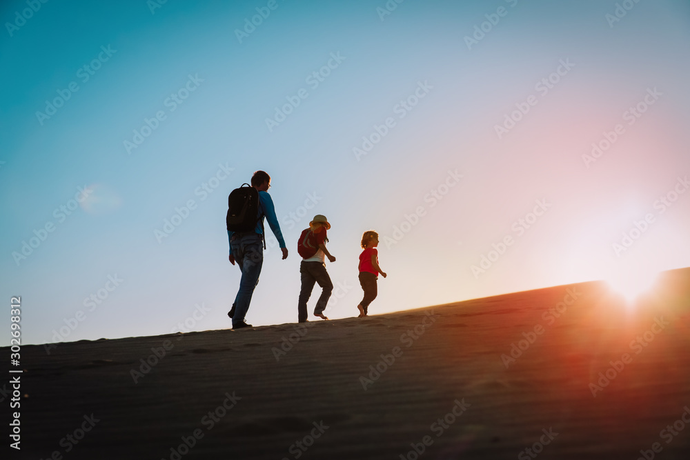 Silhouettes of father with son and daughter hiking at sunset