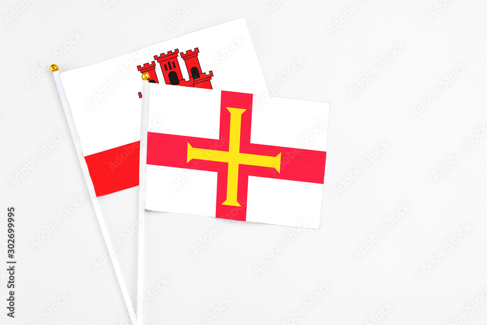 Guernsey and Gibraltar stick flags on white background. High quality fabric, miniature national flag. Peaceful global concept.White floor for copy space.