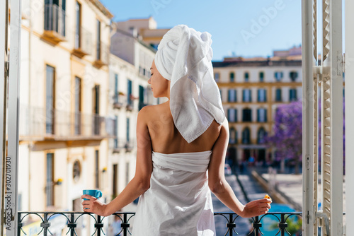 Photography hotel guest stands on the balcony with her back to the camera, drinking tea