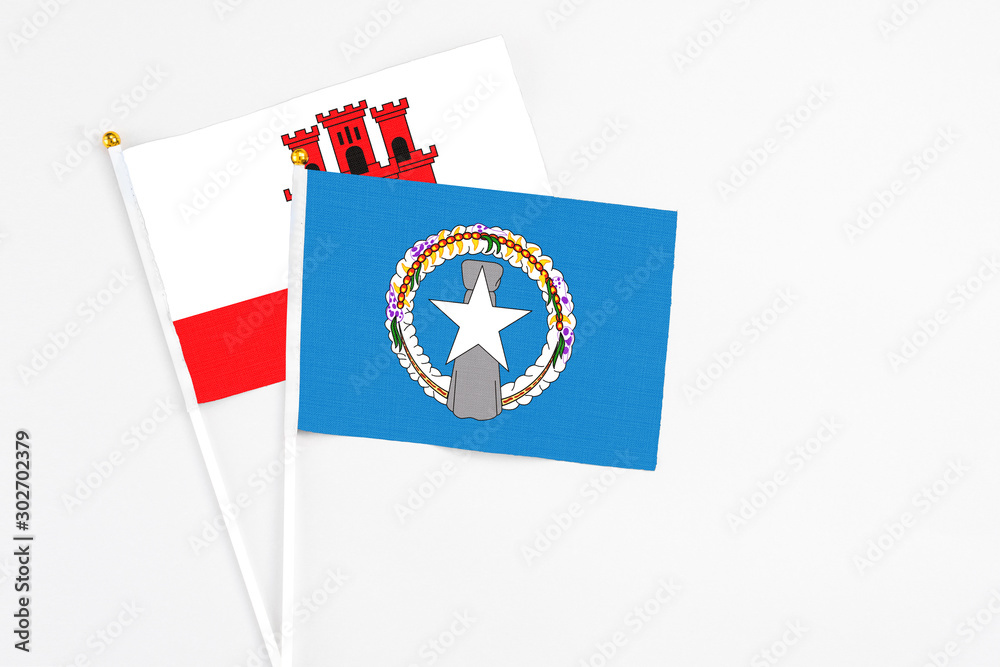 Northern Mariana Islands and Gibraltar stick flags on white background. High quality fabric, miniature national flag. Peaceful global concept.White floor for copy space.