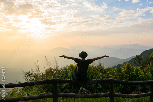 A man stands to watch the view and the sun rise in the morning sky.