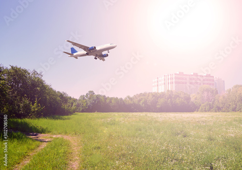 Airliner over a green field and a house in the city.