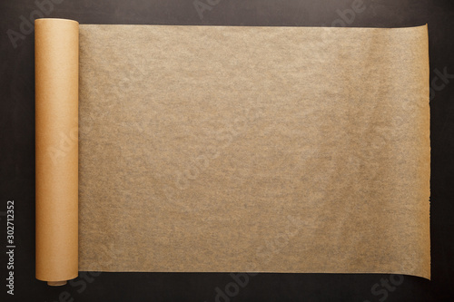 A roll of unfolded brown parchment paper, for baking food in on a dark background, top view.