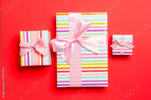 wrapped Christmas or other holiday handmade present in paper with pink ribbon on red background. Present box, decoration of gift on colored table, top view