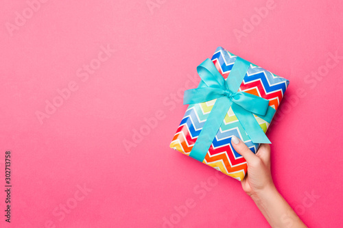 Girl Hands holding craft paper gift box with as a present for Christmas or other holiday on pink background, top view with copy sppace photo