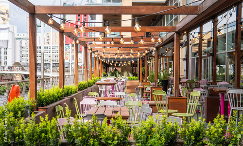 Empty tables and chairs outside a restaurant decorated with wooden bars and electric light bulbs.