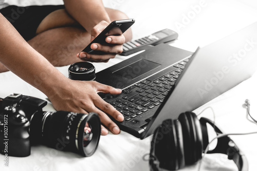 Manos de un joven en su cama revisando su teléfono mientras trabaja en su hogar photo