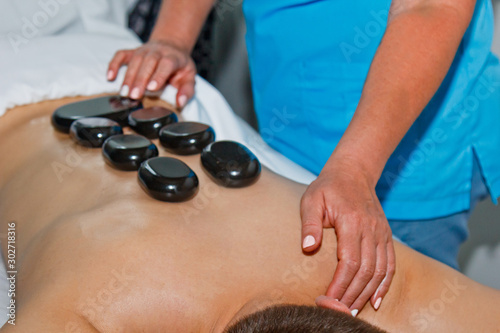 Wellness concept. Handsome young man relaxing under the stimulating effect of a traditional hot stone massage in a luxury spa and wellness center. Recovery after work.