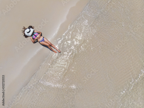 Young woman in a bikini with white hat lying on the beach on the white sand near the waves of blue sea. Top view. island, Andaman Sea, Phuket, Thailand. Aerial Shooting.