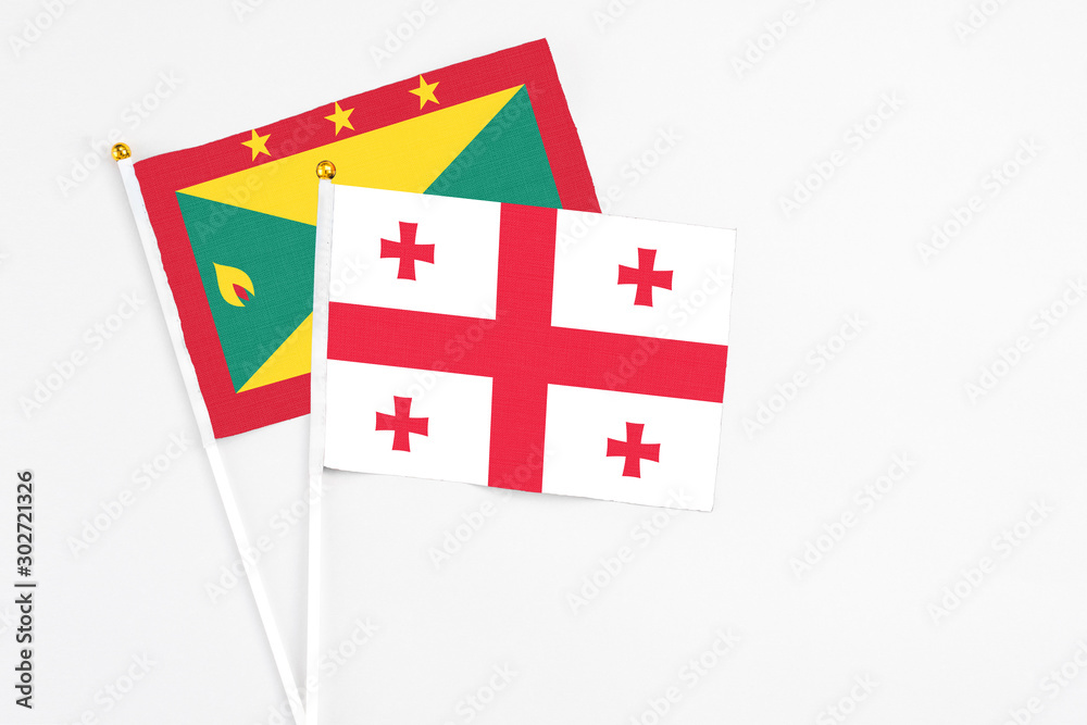 Georgia and Grenada stick flags on white background. High quality fabric, miniature national flag. Peaceful global concept.White floor for copy space.