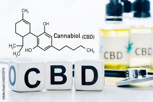 selective focus of cubes with cbd lettering near oil and stethoscope isolated on white with cbd molecule illustration photo