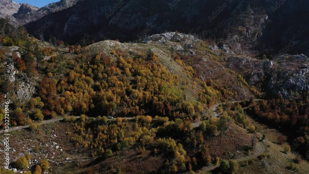 Aerial shot of a car passing by a mountain road surrounded by autumn trees, meadows and stones. Aerial shot of a car passing by a mountain road surrounded by autumn trees, meadows and stones.