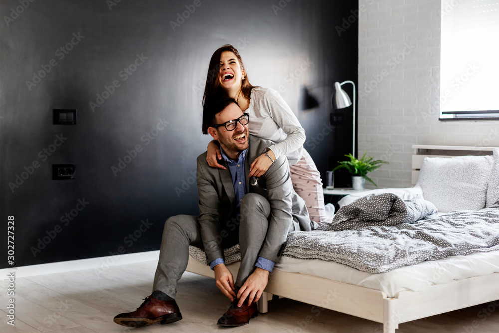 Naklejka premium Couple smile in bedroom and he prepare for work at suit and she is in pijama and hug him