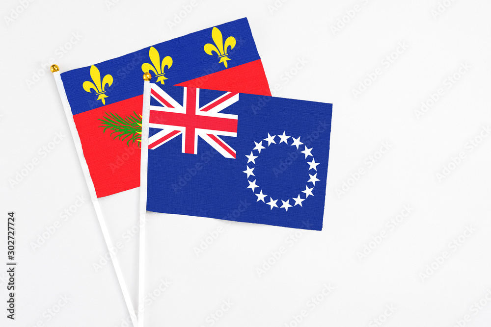 Fototapeta premium Cook Islands and Guadeloupe stick flags on white background. High quality fabric, miniature national flag. Peaceful global concept.White floor for copy space.