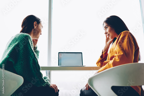 Slika na platnu Below view of two skilled students having friendly conversation sitting at modern netbook with blank screen area for advertising
