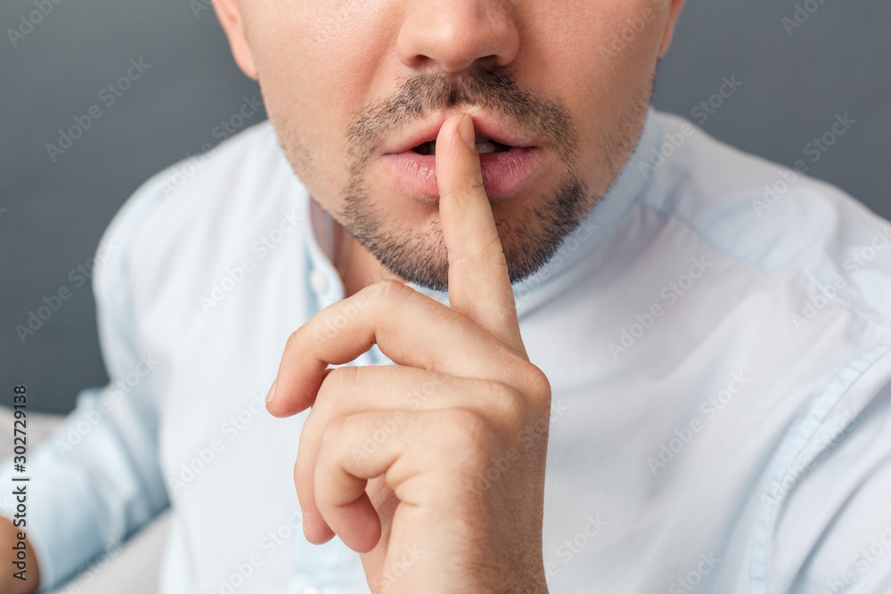 Be Quiet. Young man studio sitting on sofa isolated on grey showing hand gesture close-up Be Quiet. Young man studio sitting on sofa isolated on grey showing hand gesture close-up