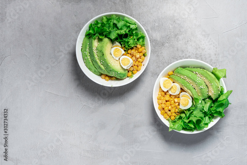 Healthy salad made of avocado, lettuce, seeds, corn and quail eggs in white bowls, top view, free space for text. Healthy lacto-ovo-vegetarian food. Salad with avocado on a grey background, copy space photo