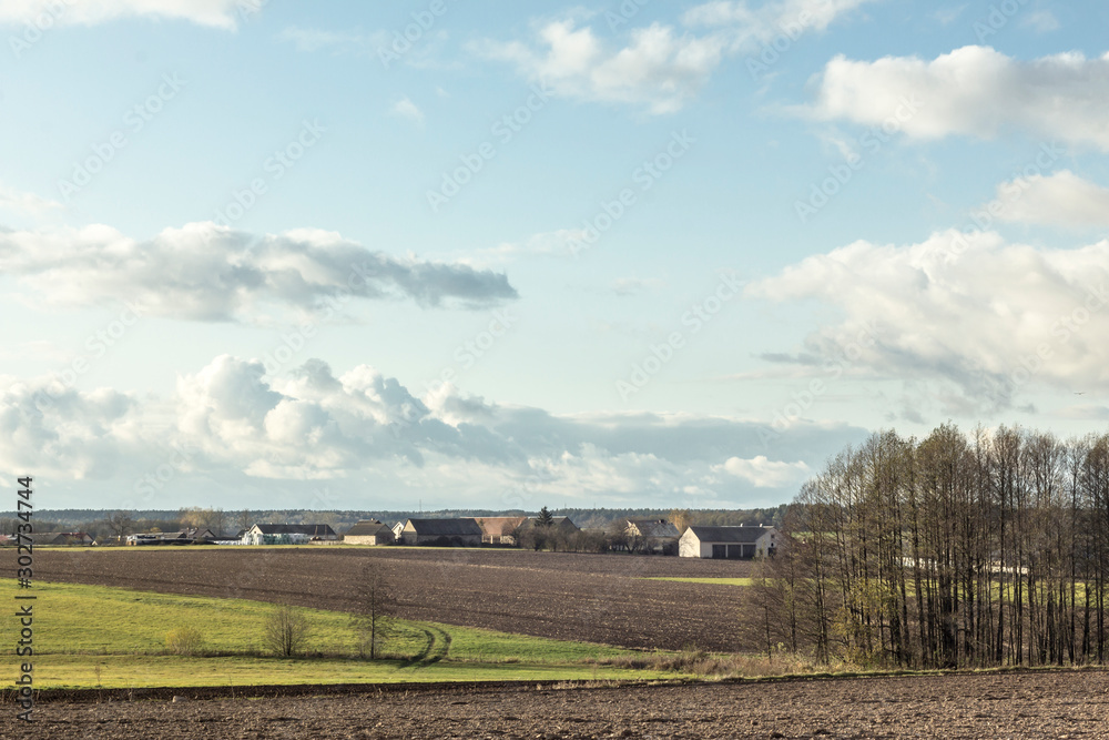 View of the village from the plowed fields. Residential buildings, barns, equipment. Trees in the foreground. Podlasie. Poland.