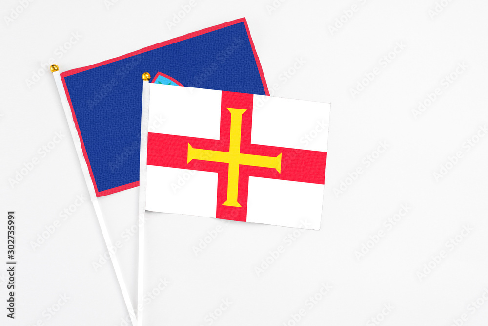 Guernsey and Guam stick flags on white background. High quality fabric, miniature national flag. Peaceful global concept.White floor for copy space.