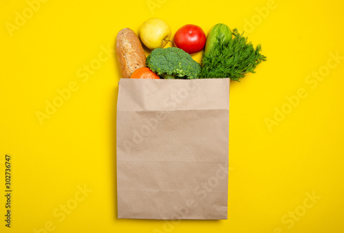 Food vegetable, bread, fruit in paper bag package on yellow background, top view