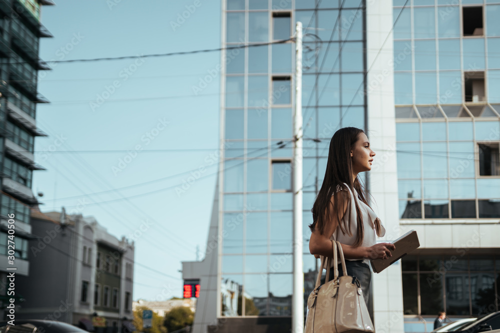girl with a tablet pc in hands is walking along a city street against the background of glass skyscrapers girl with a tablet pc in hands is walking along a city street against the background of glass skyscrapers