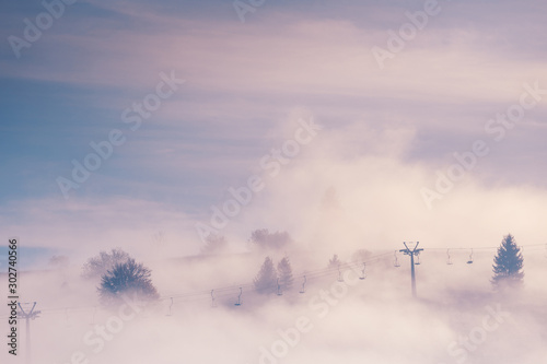Beautiful scenery of spruce trees and .ski elevator on the mountain hills sticking out through the morning fog at beautiful autumn foggy sunrise. Carpathian mountains. Ukraine. © stone36