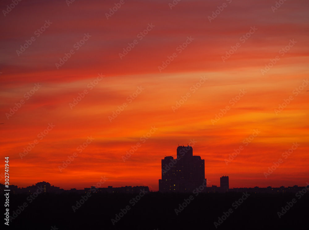 Skyscraper tower silhouette over dark forest on sunset and colorful orange tone sky with long clouds as background. Sunny weather (Moscow city, Russia)