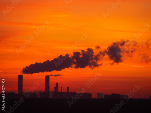 Tall smoking chimneys from industrial plant and far buildings behind the dark forest. Cityscape silhouette with colorful twilight sky on sunset. Moscow city  Russia.