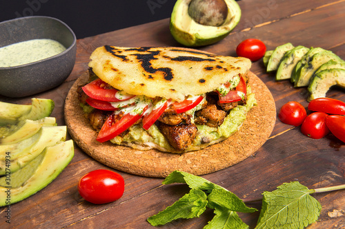 Arepas - Traditional Colombian Food originally from Latin America arranged on a old rustic wooden table mixed with meat, vegetable and special avocado sauce photo