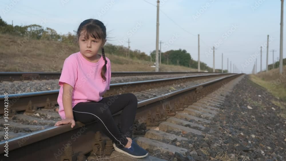 Sad child on the railway. Loneliness of the child. Sad little girl alone sits on the railroad. Abandoned child concept.