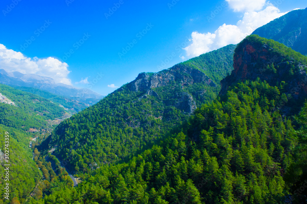 Top view of high mountains covered by forest, blue sky with white clouds on a sunny summer day.