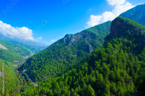 Top view of high mountains covered by forest  blue sky with white clouds on a sunny summer day.