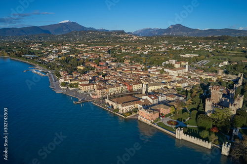 Aerial view of Lake Garda and the city center of Lazise, Italy. Autumn season, blue sky, Monte Baldo on the horizon, snow in the mountains