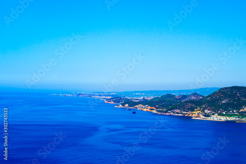 Blue sea, clear cloudless sky and shore with green hills, top view.