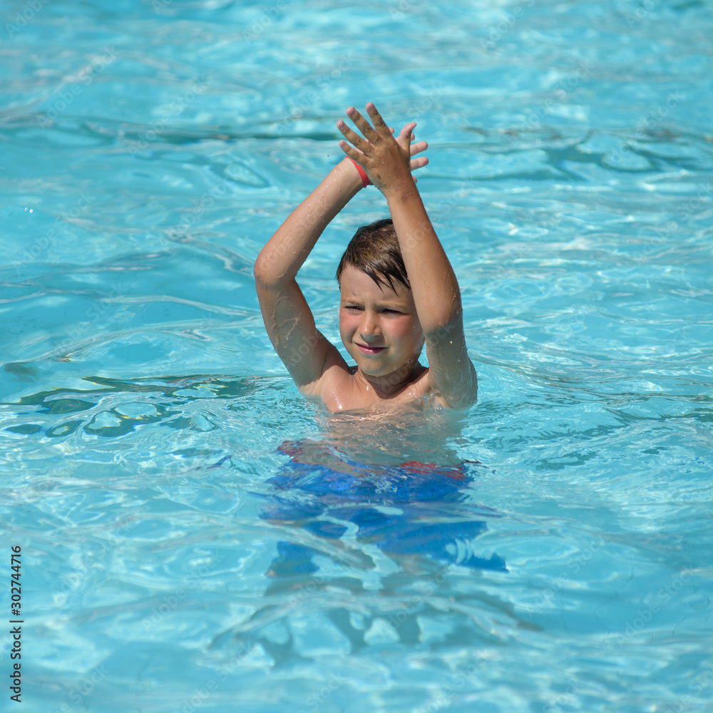Fitness, healthy lifestyle. Cute European boy dancing aqua Zumba at hotel’s pool, he having fun during his summer holidays. He repeating movements by animator.