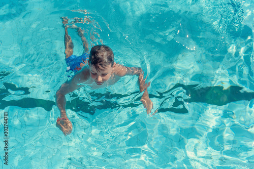 Learning to swim. Boy swimming along the side of pool. © Artem
