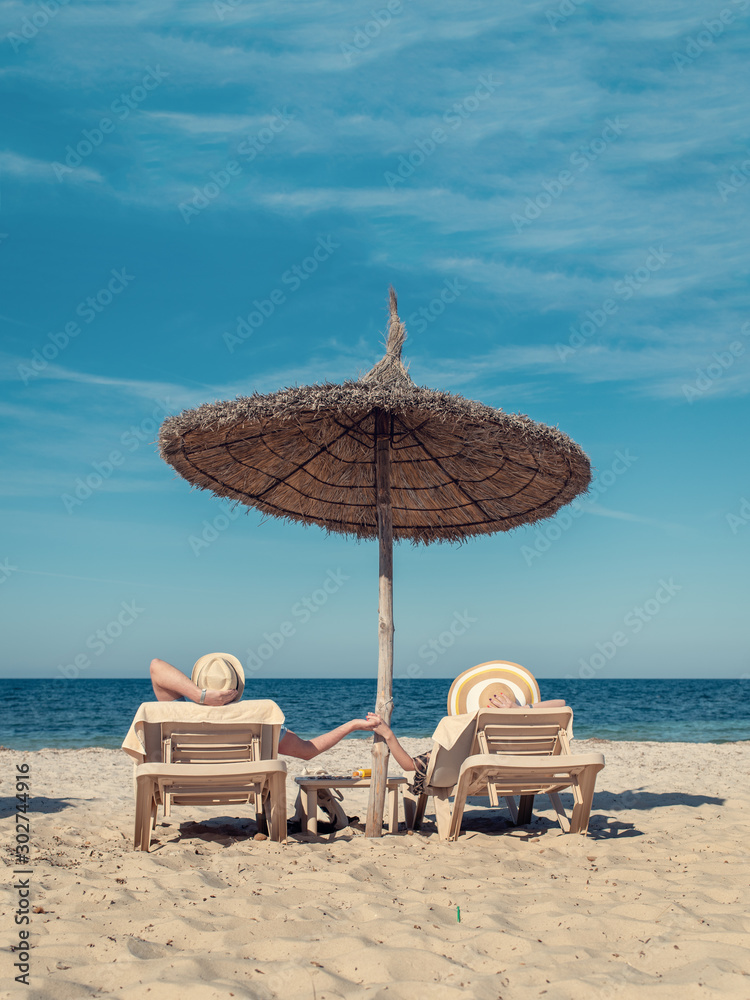 Rest on Tropical Island. Young European family is enjoying their summer holidays, laying on sunbeds at beach of luxurious hotel.