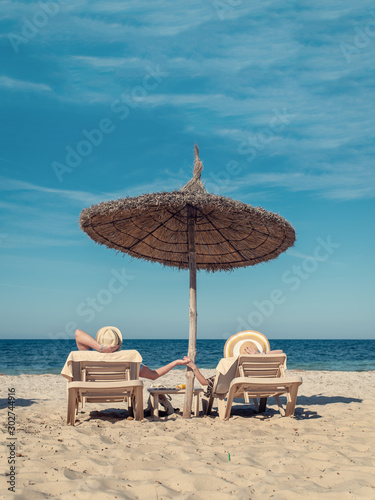 Obraz na płótnie Rest on Tropical Island. Young European family is enjoying their summer holidays, laying on sunbeds at beach of luxurious hotel. w salonie