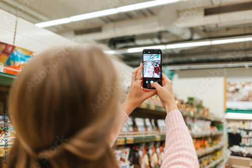 Mobile and social network. lond woman taking a selfie on smartphone in the grocery store. Rear view from the head photo