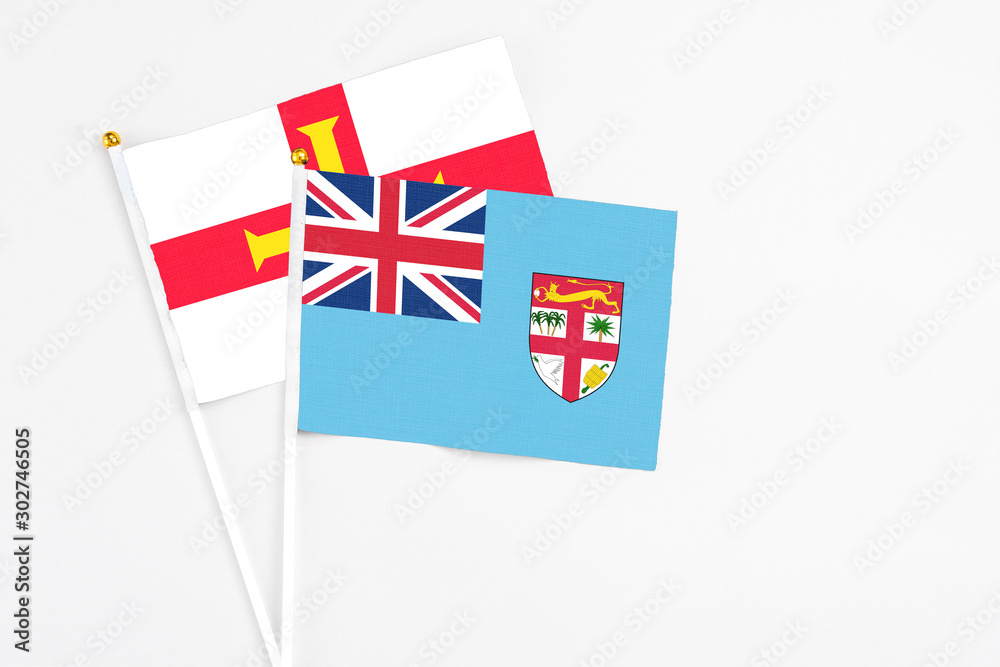 Fototapeta premium Fiji and Guernsey stick flags on white background. High quality fabric, miniature national flag. Peaceful global concept.White floor for copy space.