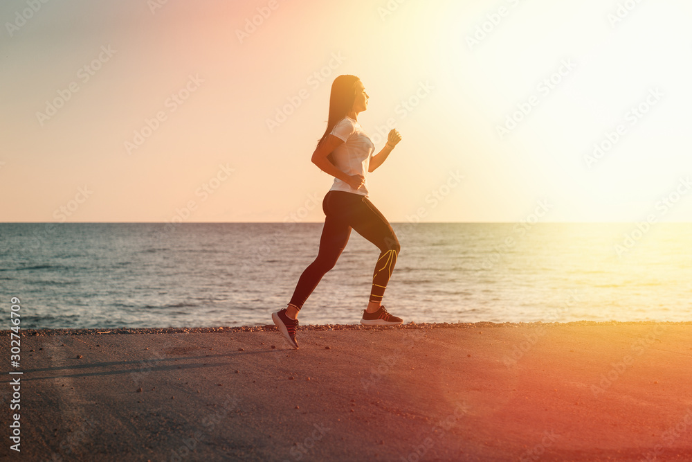 Sports and Jogging along the sea. A young brunette woman runs along the path along the seashore. In the background, the sea and sky in the setting sun. Copy space