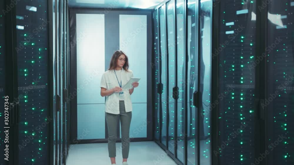 Female IT engineer performing data center backups with digital laptop. Cheerful woman administrator working in high tech rack server room. Female IT engineer performing data center backups with digital laptop. Cheerful woman administrator working in high tech rack server room.