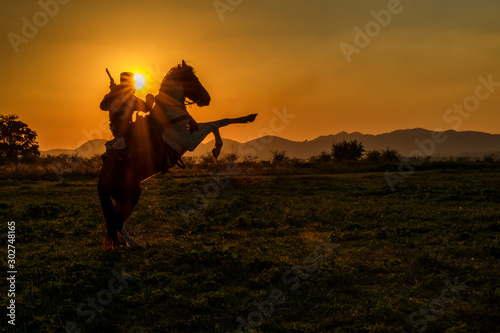 Silhouette of cowboy man riding horseback jumping at sunset and mountain background