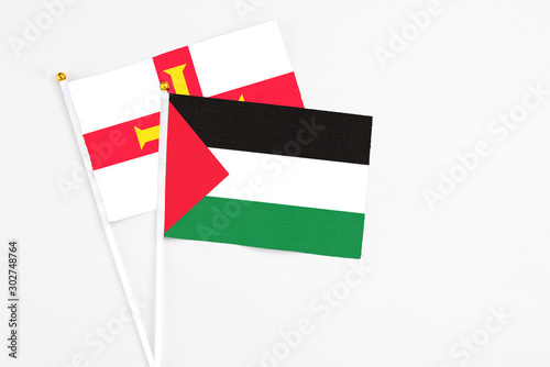 Palestine and Guernsey stick flags on white background. High quality fabric, miniature national flag. Peaceful global concept.White floor for copy space. photo