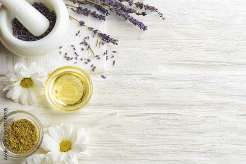 Composition with dried lavender flowers in white marble pestle and mortar and natural chamomile oil cosmetic in glass jar on white background, top view with free copy space