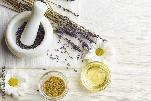 Composition with dried lavender flowers in white marble pestle and mortar and natural chamomile oil cosmetic in glass jar on white background, top view with free copy space