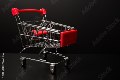Closeup of a miniature red shopping cart on a black background. 