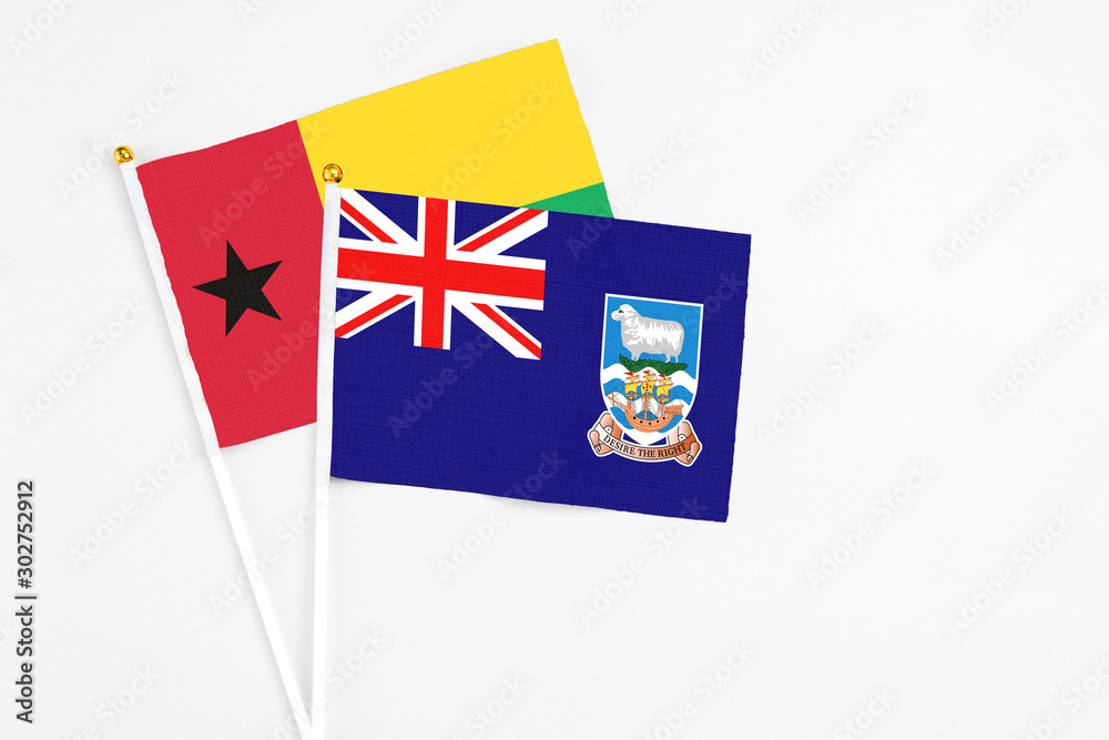 Fototapeta premium Falkland Islands and Guinea Bissau stick flags on white background. High quality fabric, miniature national flag. Peaceful global concept.White floor for copy space.