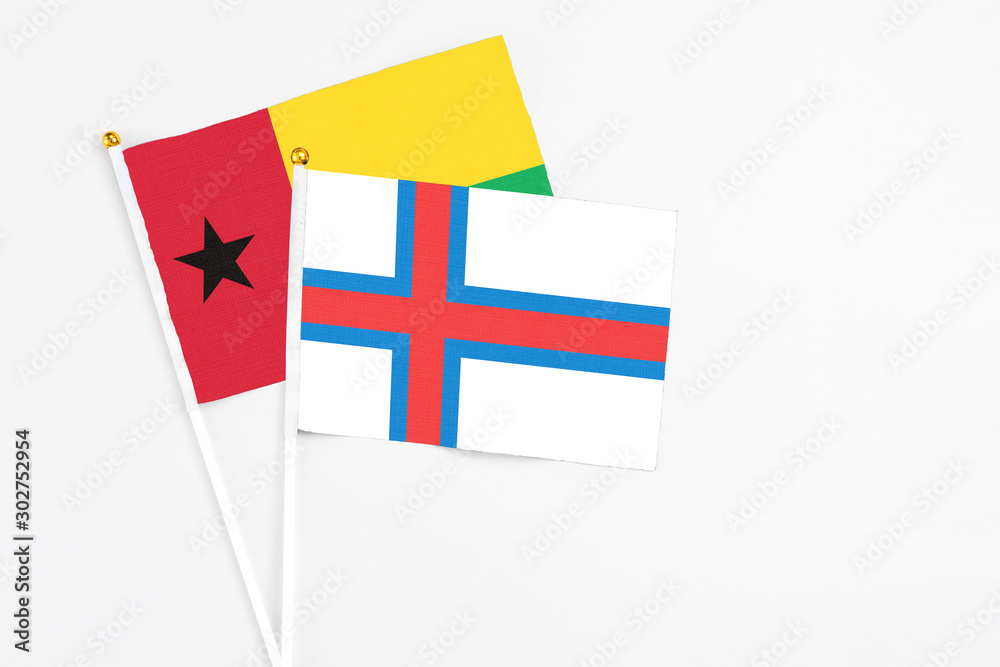 Faroe Islands and Guinea Bissau stick flags on white background. High quality fabric, miniature national flag. Peaceful global concept.White floor for copy space.